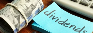 a pack of dollar notes next to a sticky note with the word "dividends" written on it